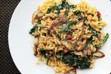 Overhead shot of a plate of pasta tossed with pancetta, mushrooms, and wilted greens