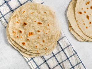 Mexican-style flour tortillas stacked on a blue-striped white kitchen towel