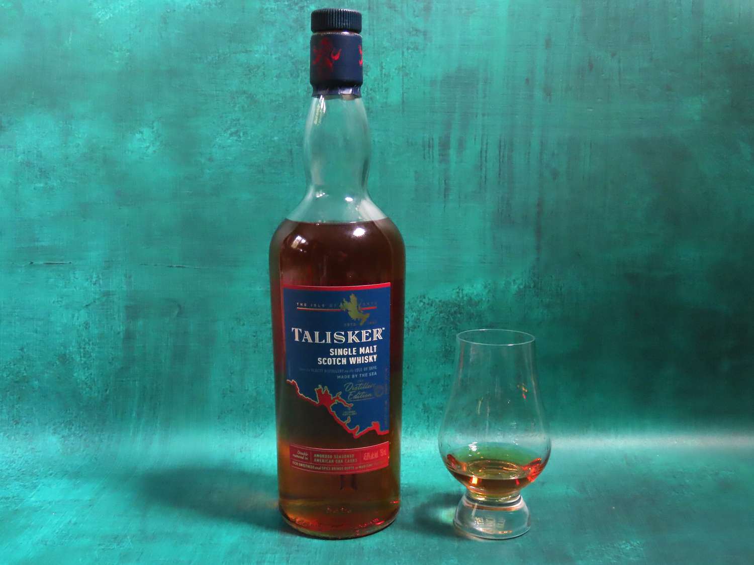 a bottle of Talisker distiller's edition on a blue background with a glass of whisky beside it