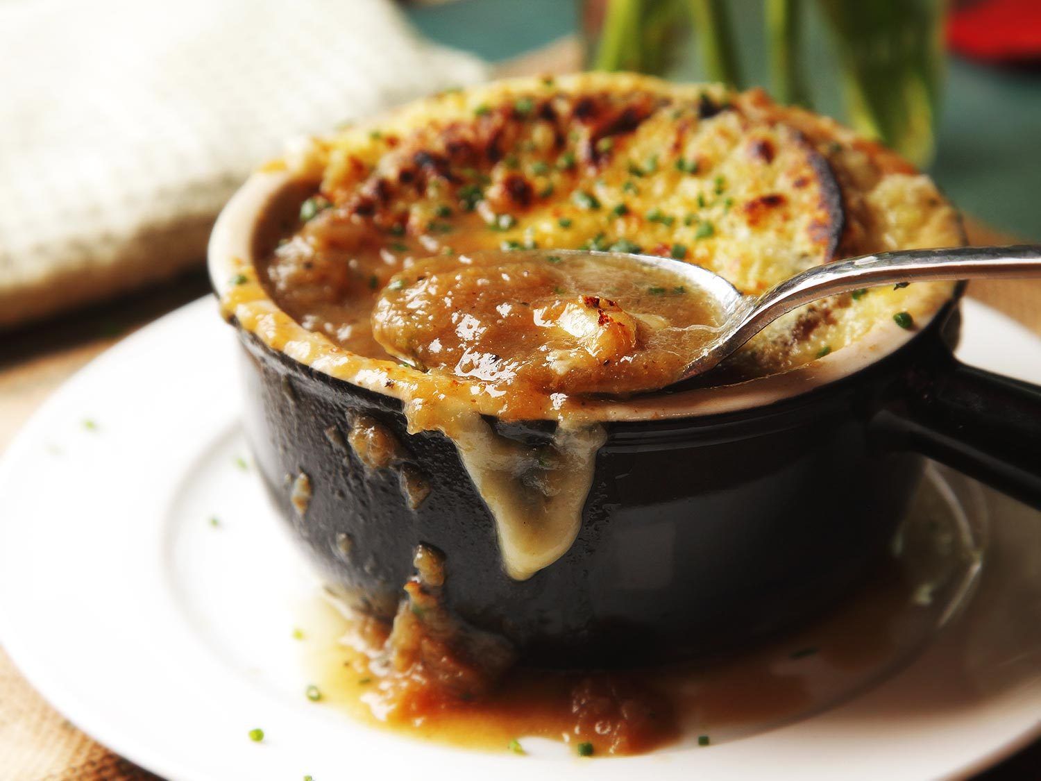 Spoon lifting caramelized onions out of crock of pressure cooker french onion soup.