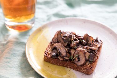 A slice of Danish rye bread toast topped with sautéed mushrooms, next to a glass of beer