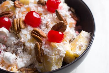 A bowl of ambrosia, a fruit salad with coconut, pineapple, pecans, mini-marshmallows, and cherries.