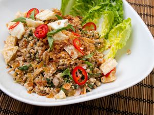 Pork larb, served in a white bowl with leaves of romaine lettuce on the side.