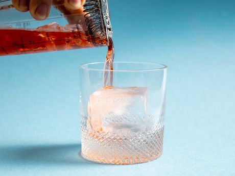 a cocktail being poured over a large ice cube in a rocks glass