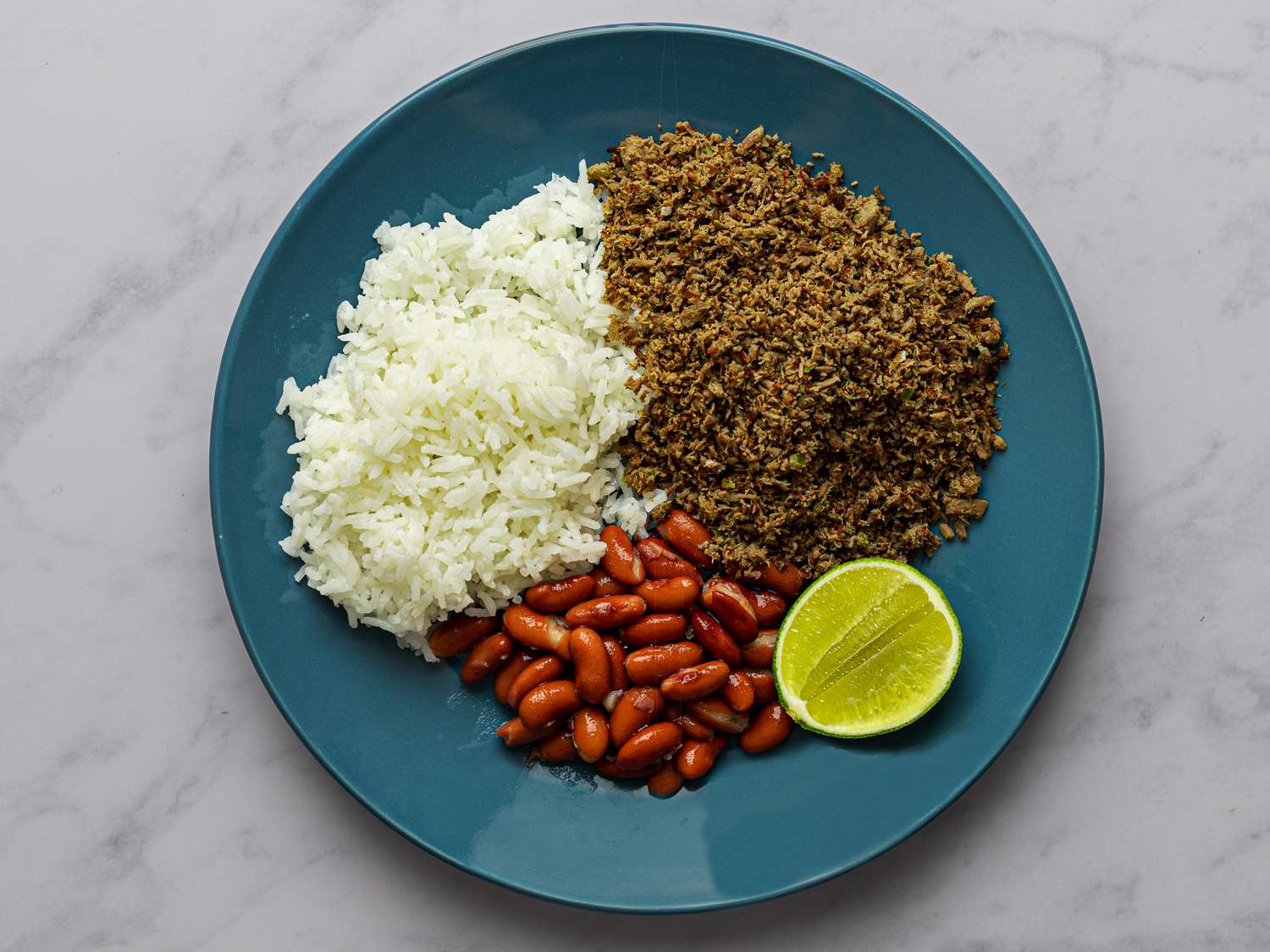 SalpicÃ³，白米饭，红芸豆和一片酸橙放在大理石柜台上的蓝色盘子里。gydF4y2Ba