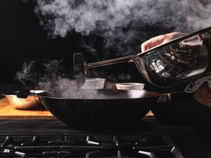 A lid being removed off a smoking wok