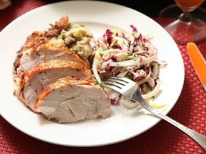 Thick slices of perfectly cooked roast turkey breast arranged on a white plate, along with stuffing and a radicchio salad.