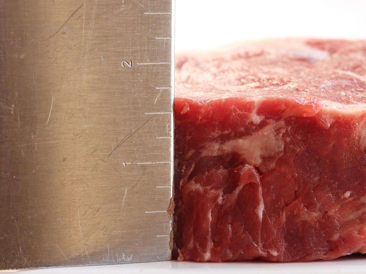 A ruler measuring the thickness of a thick-cut raw steak
