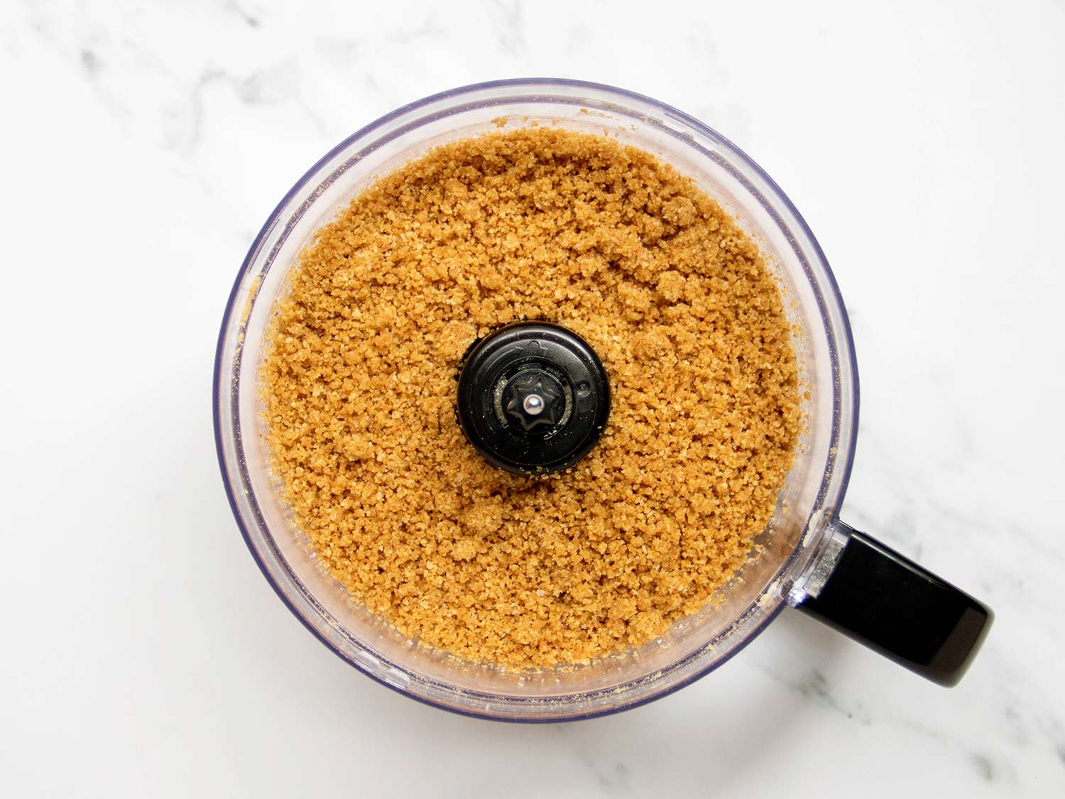 Vegan graham crackers and vegan butter blended in bowl of food processor