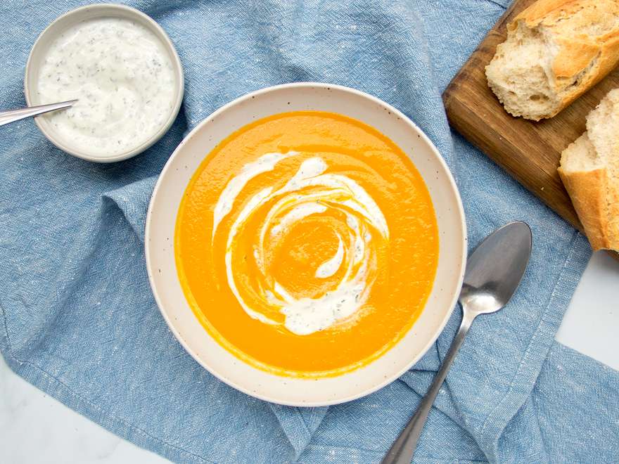 用勺子舀胡萝卜汤到一个白色的碗里。