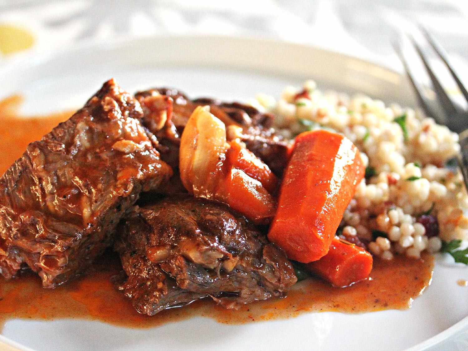 A closeup shot of Moroccan pot roast plated with carrots and couscous