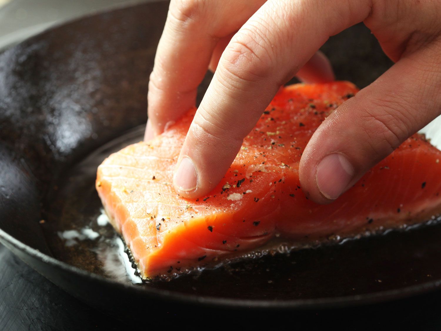 将带皮的鲑鱼片压入热油锅中，表皮朝下。