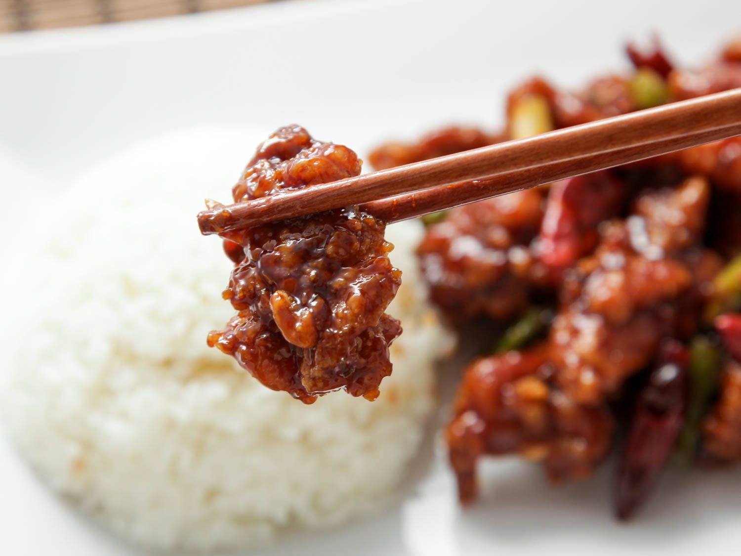 Using chopsticks to hold a piece of General Tso's chicken over a bed of rice, with more chicken in the background.