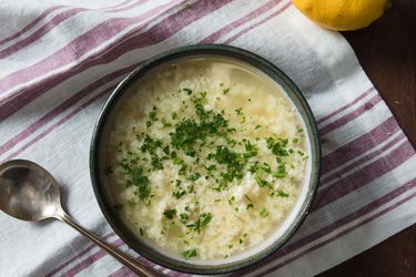 Bowl of stracciatella soup on a purple and white striped towel with a spoon on the side.