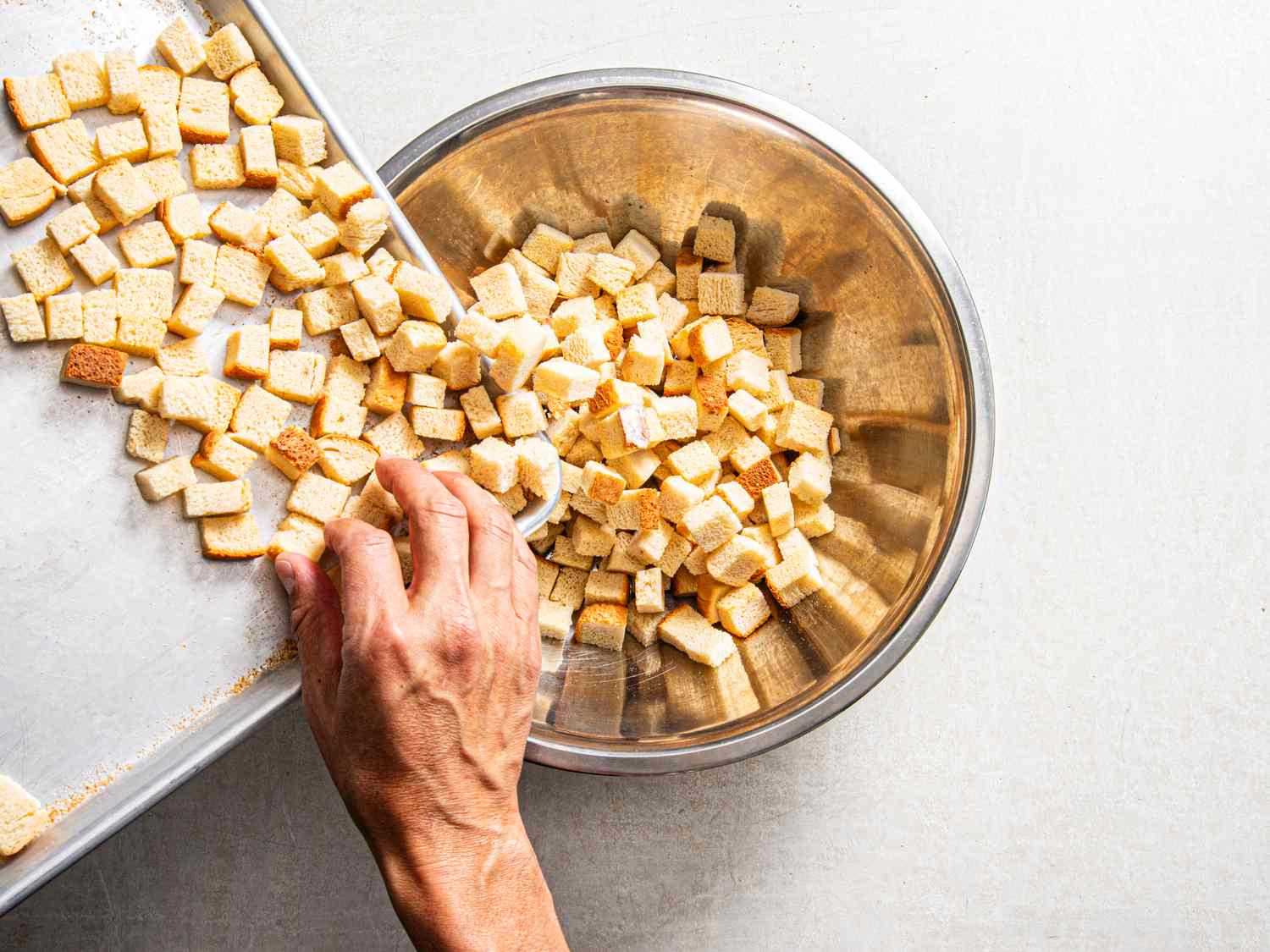 Overhead view of transferring bread cubes to bowl