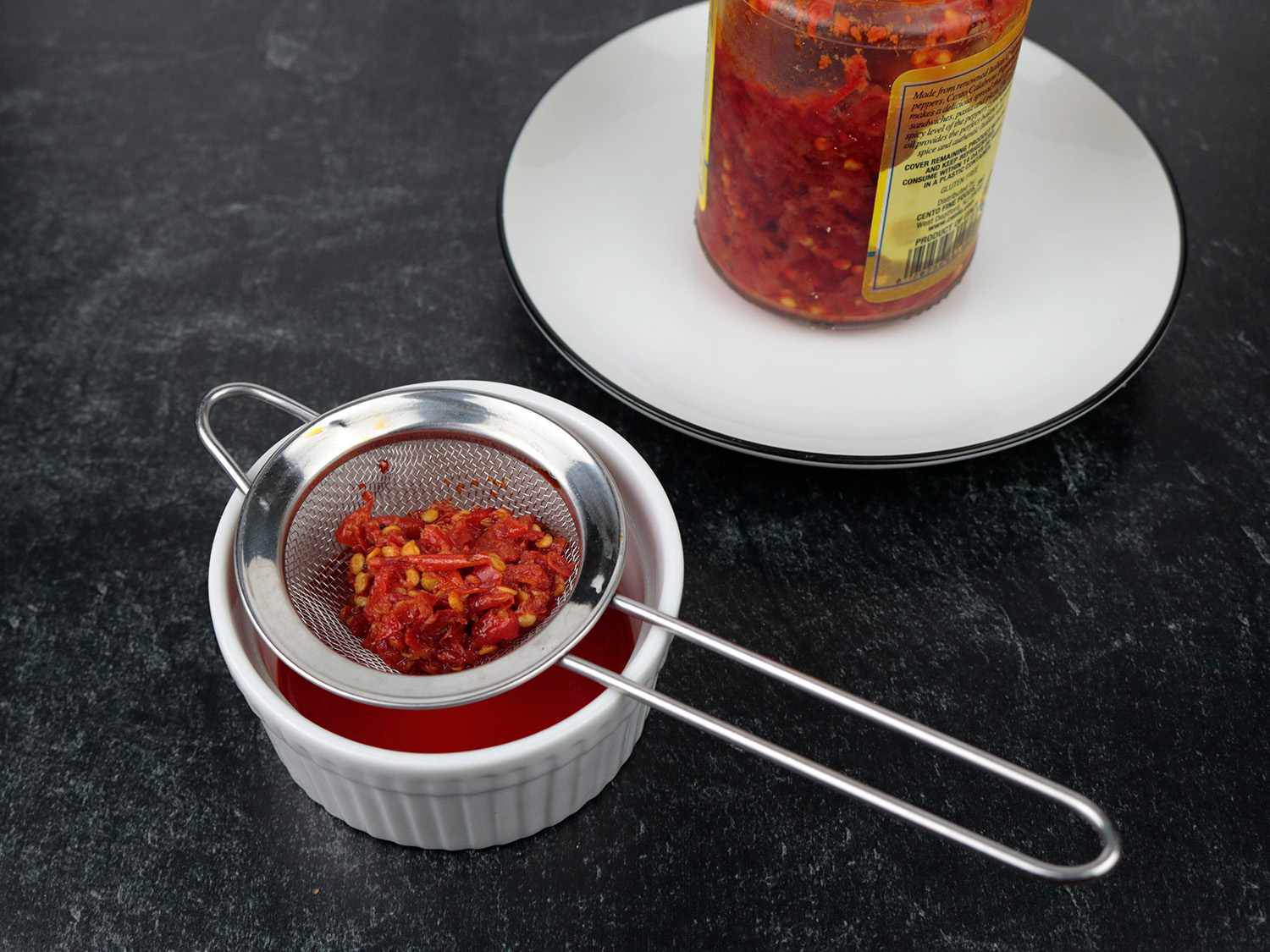 a small fine mesh strainer drains hot peppers of their oil