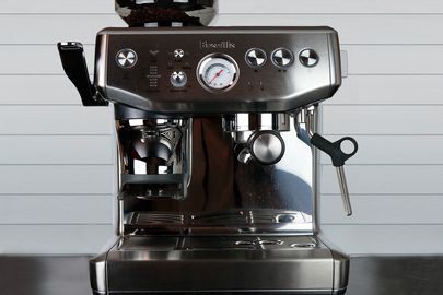 an espresso machine with a built-in grinder sits on a counter in front of a tiled wall