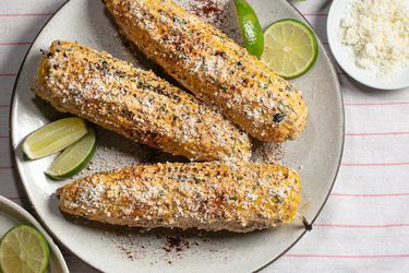 elotes(grilled Mexican street corn) on a plate with limes and chili powder