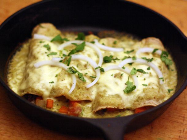 A skillet of enchiladas suizas stuffed with vegetables and topped with sliced onion and cilantro.