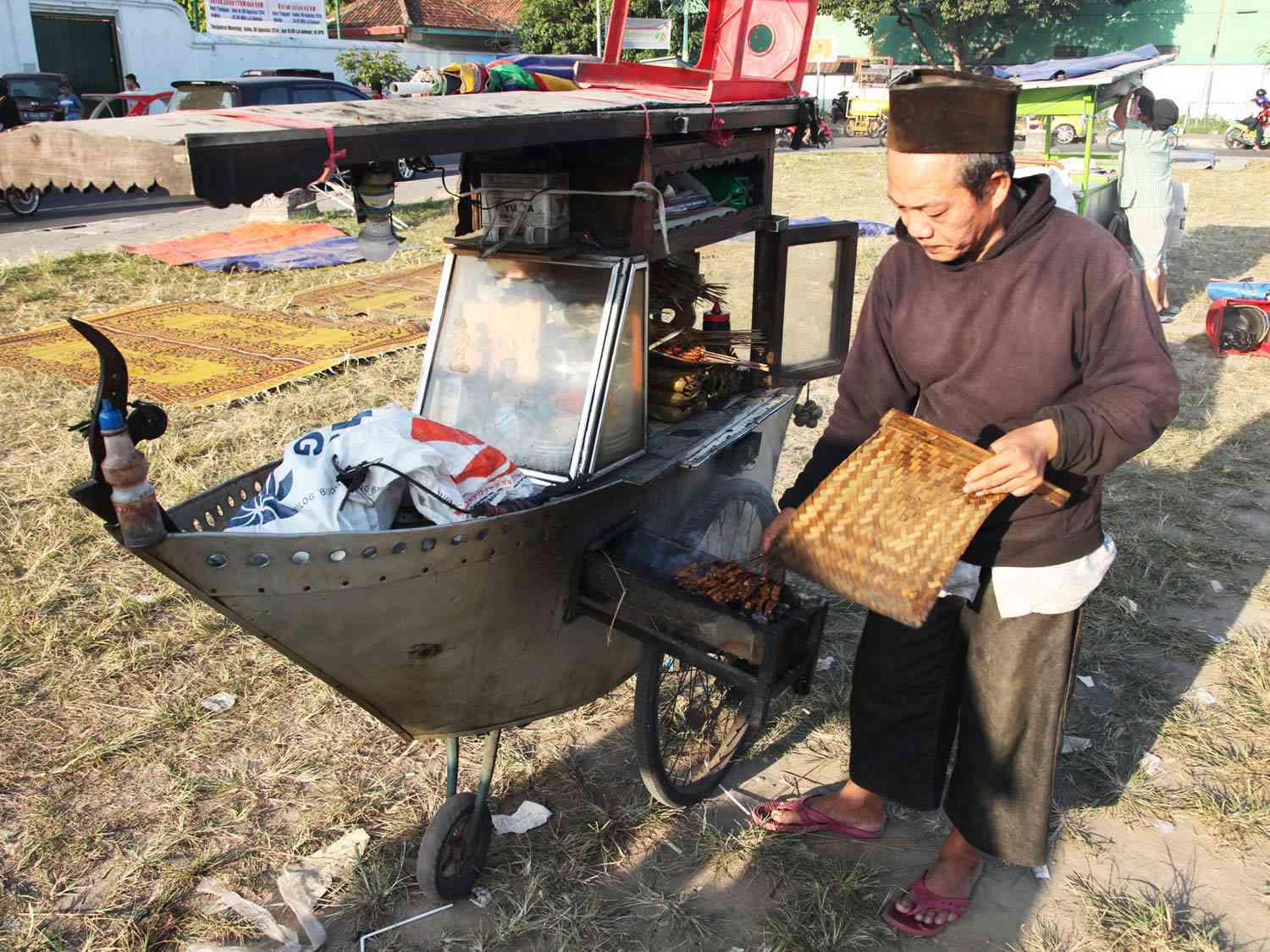 印尼雅加达，一名卖沙爹牛肉的小贩站在一辆装有烤架的船形推车旁