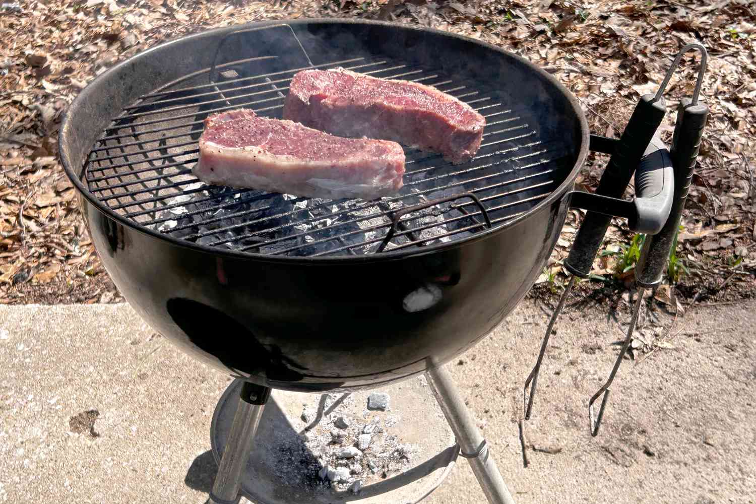 two steaks cooking on a charcoal grill