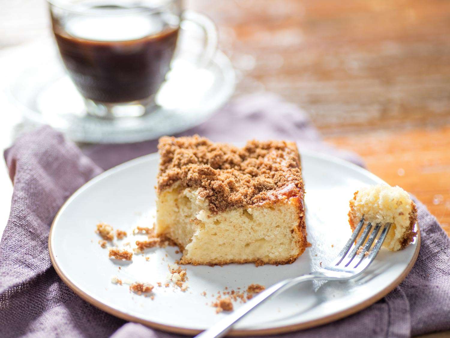 A piece of coffee cake on a serving plate; a fork has taken a corner of the cake out of it.