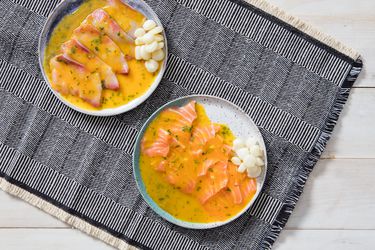 两个形成边缘的顶视图,斑纹d plates of Peruvian tiradito with aji amarillo and lime, set on a woven, patterned cloth.