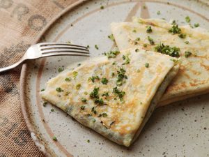 Two quarter-folded filled crepes garnished with chopped herbs on a plate