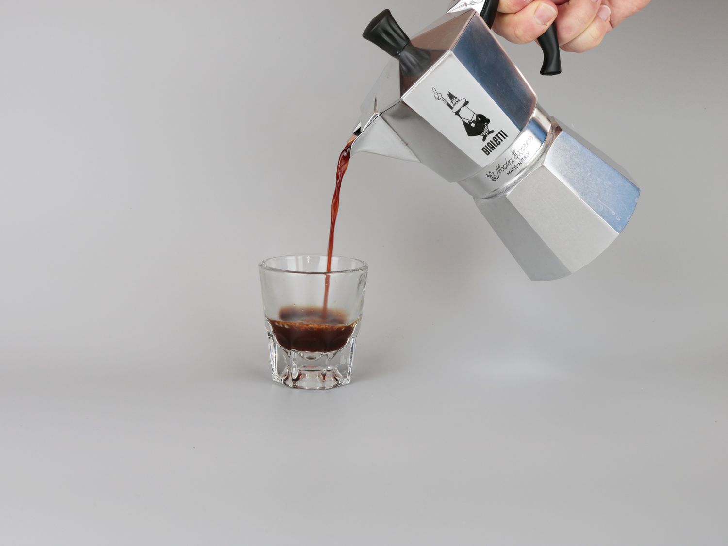 a moka pot pouring coffee into a glaass