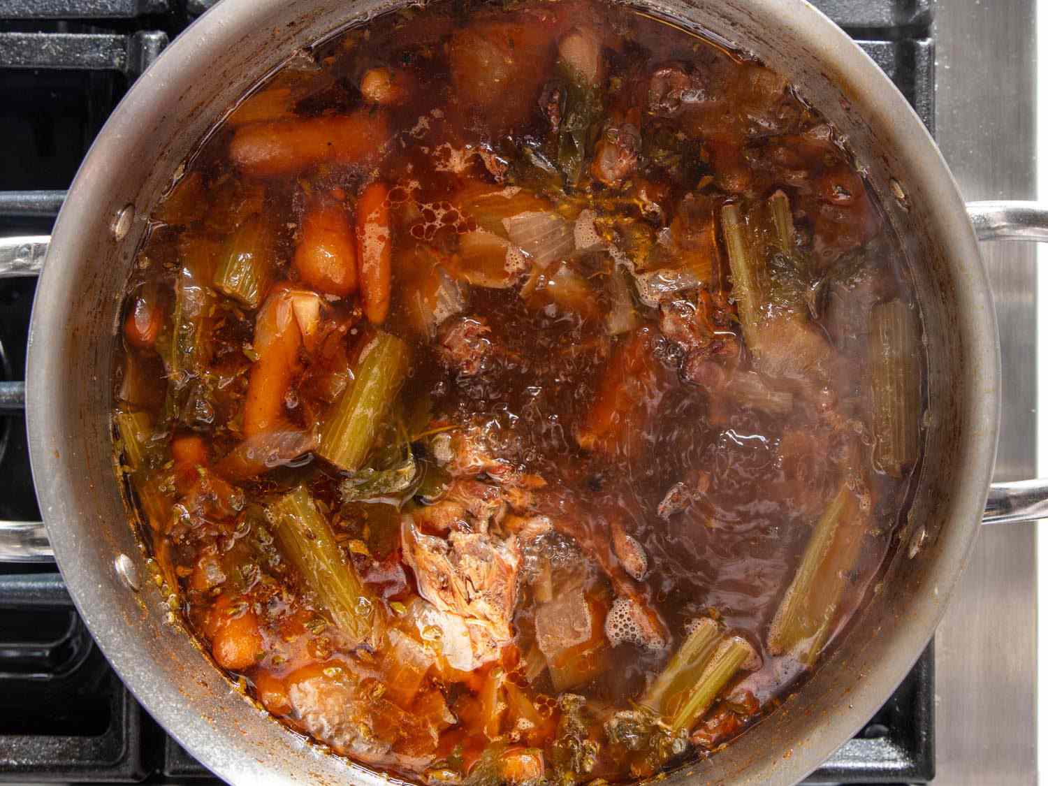 Closeup overhead of duck stock simmering in a stockpot.