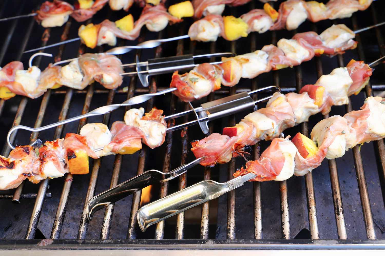 numerous skewers cooking on a gas grill