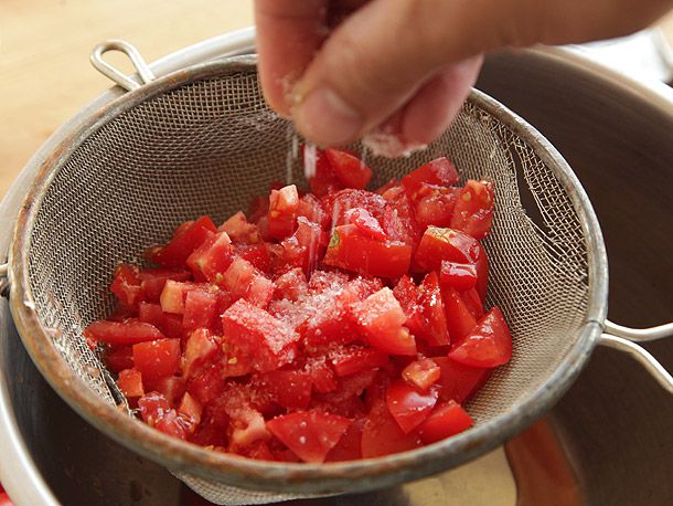一只手将盐撒在一堆用细孔过滤器切碎的西红柿上