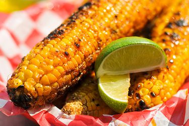 Corn with chili lime butter and lime wedges on a paper plate.