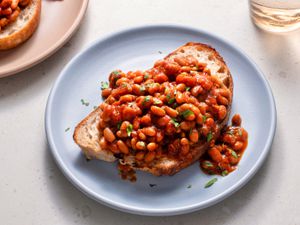 British-style baked beans on a piece of white bread which is placed on a blue ceramic plate on a stone background