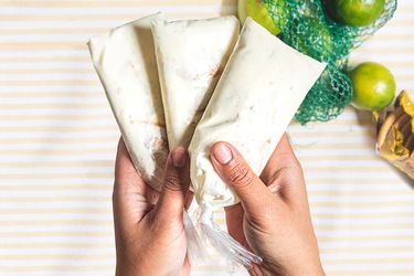 Overhead view of two hands holding three key lime bolis over a bag of limes and maria cookies