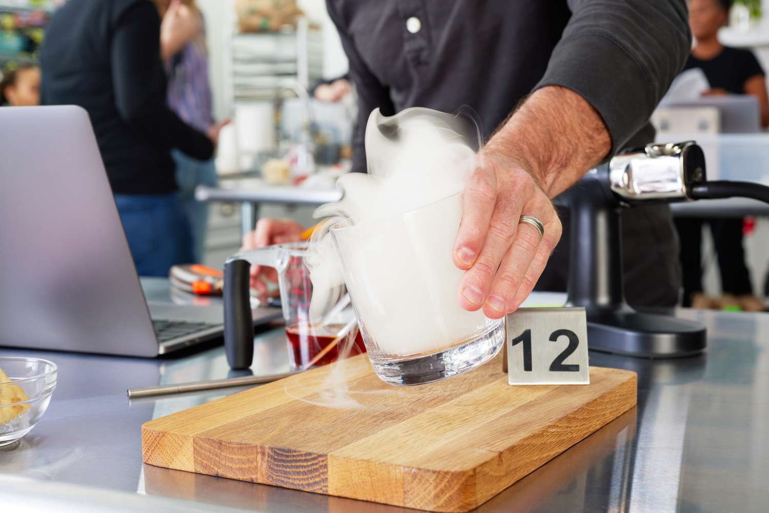 A hand holding a cocktail glass that smoke is rising out of