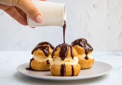 A trio of profiteroles being doused in chocolate sauce