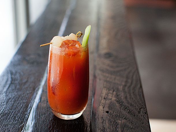 A Bloody Mary cocktail in a tall glass garnished with a celery stick and some shrimp on a toothpick.