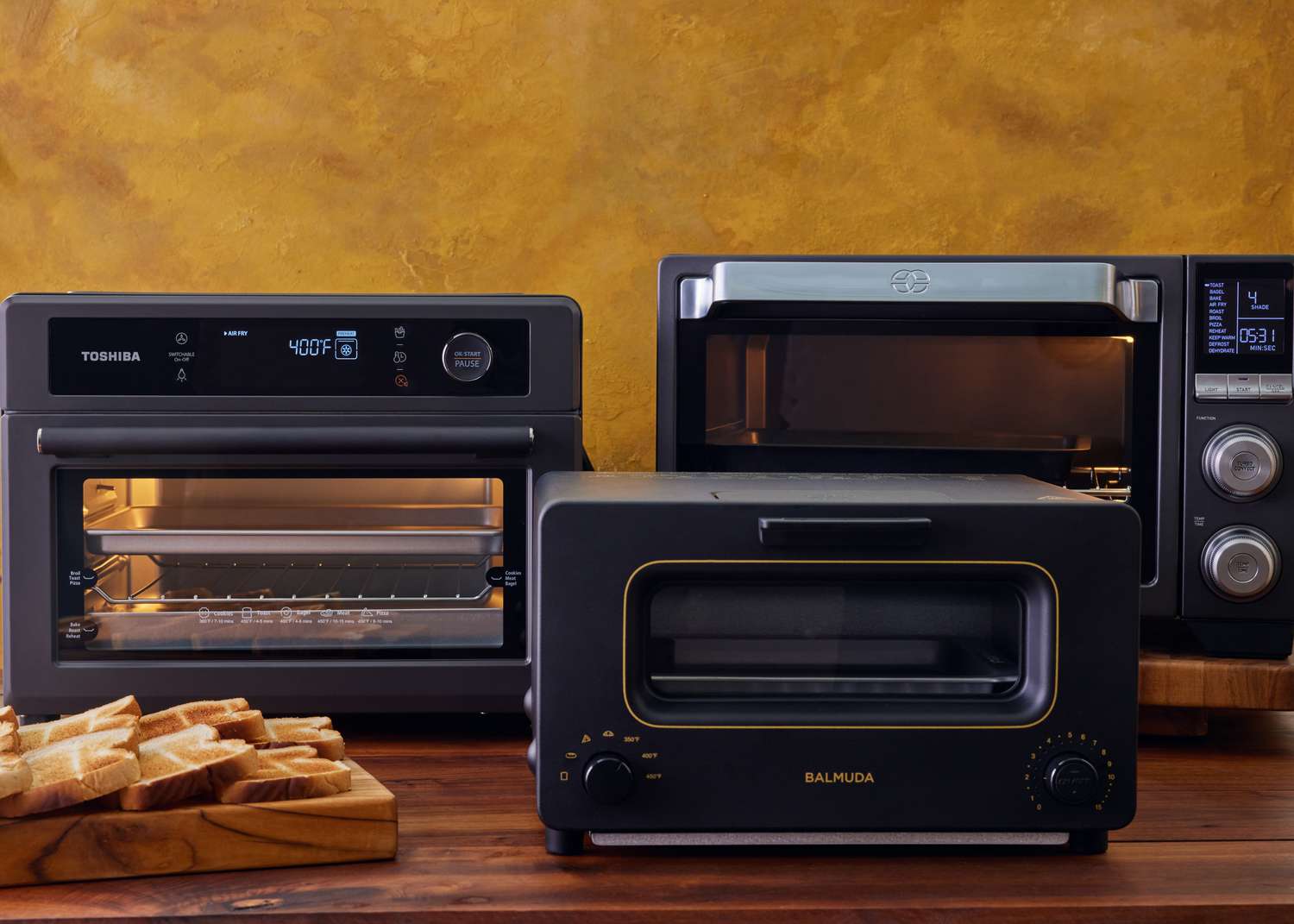 Three air fryer toaster ovens on a wooden countertop