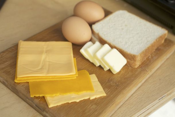 几片奶酪(美式和切达干酪)，两个鸡蛋，四片黄油，两片面包放在木砧板上