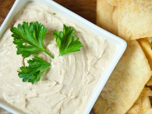 Overhead closeup of a square bowl of hummus, garnished with a large parsley sprig.