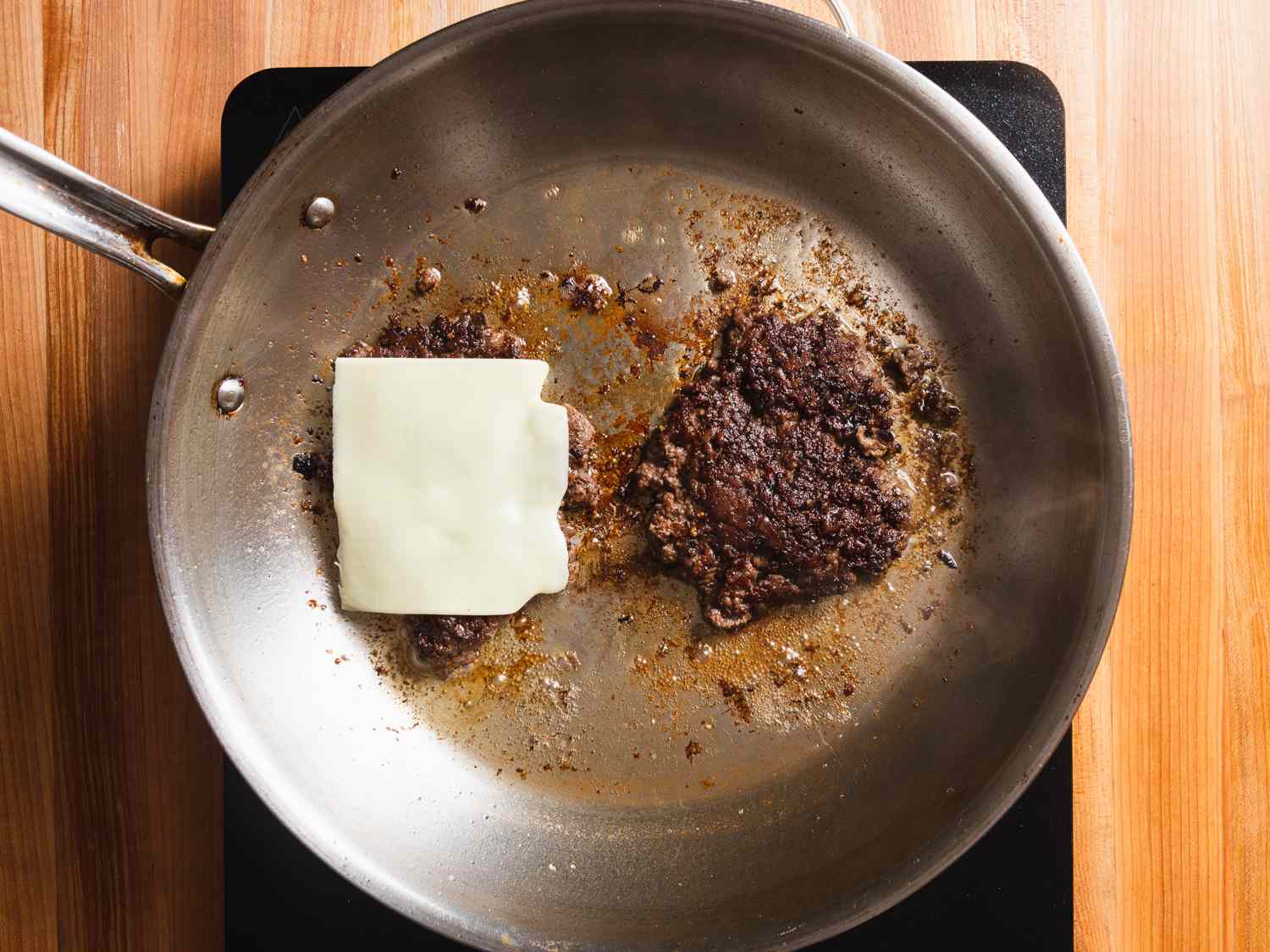 在热煎锅中翻动后将汉堡捣碎，露出深棕色的外壳，并在一块肉饼中加入奶酪。＂width=