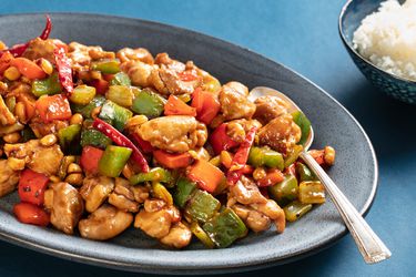 Takeout-style kung pao chicken on a grey plate with rice on the side.