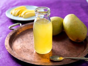 Open bottle of homemade mango syrup with fresh mangoes