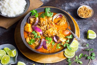 Chicken massaman curry with wheat beer and potatoes, served in a gray bowl alongside rice and lime wedges.