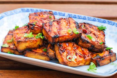 A platter of grilled marinated tofu with chipotle-miso sauce garnished with chopped scallion.
