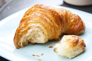 A croissant, torn open to display its interior, on a blue plate.