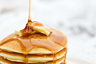 A stack of pancakes with butter on top and syrup being poured over them.