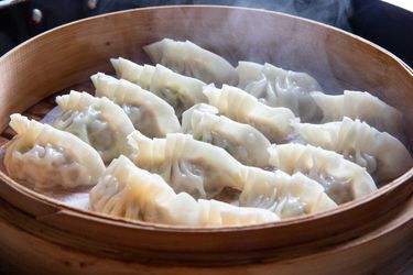 Homemade pork and scallion dumplings in a bamboo steamer.