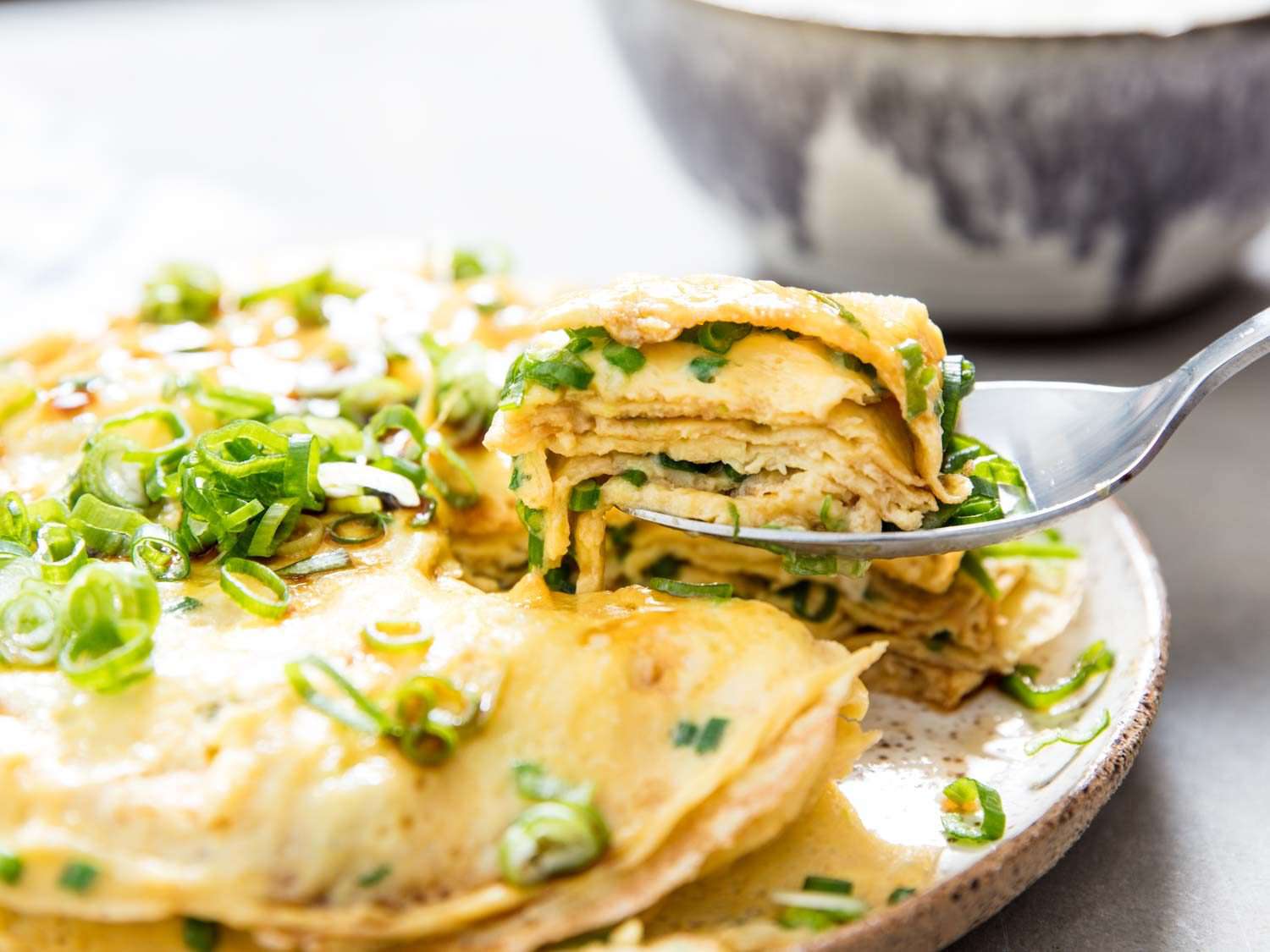 Taking a bite with a fork of a layered omelette topped with scallions.